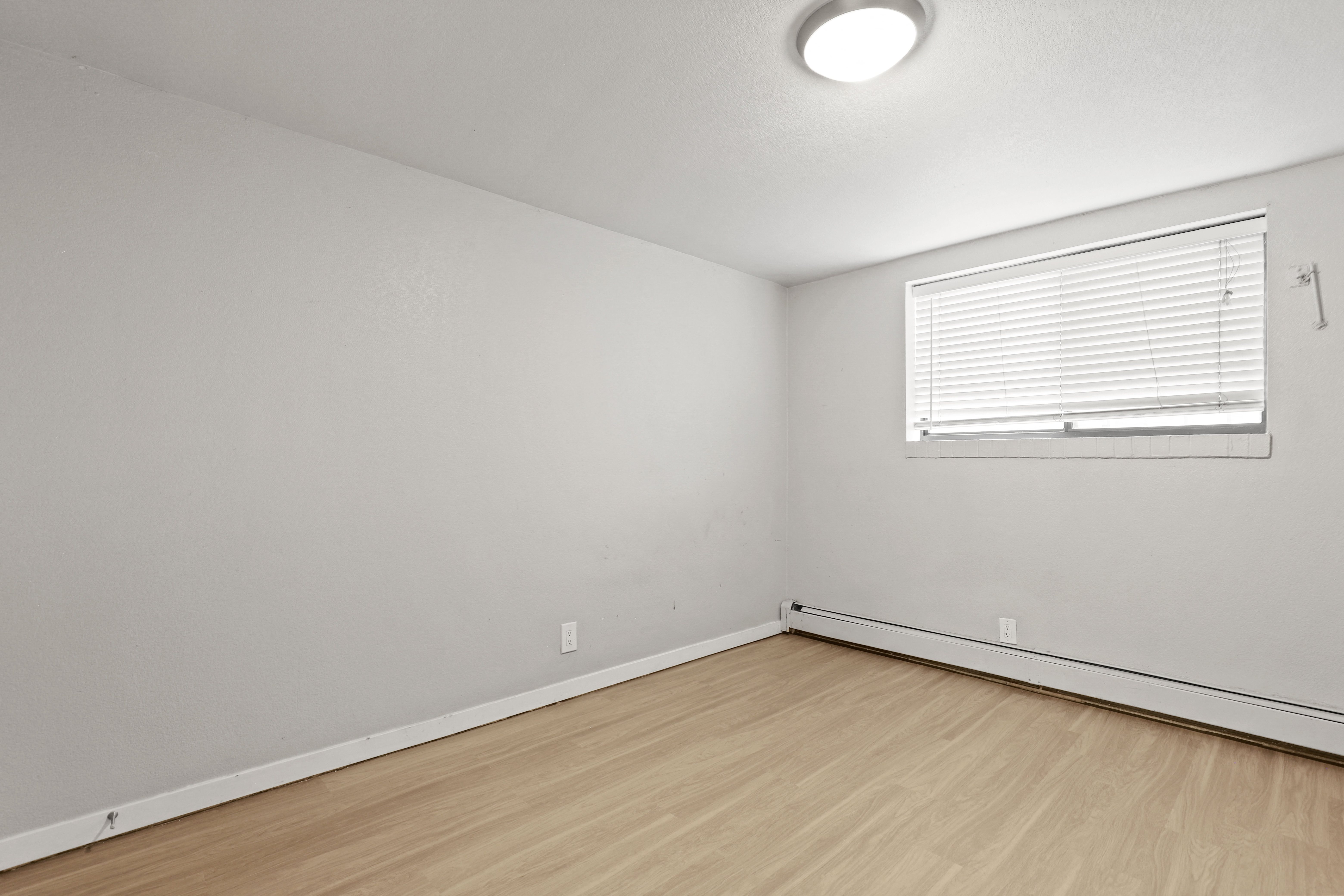 a bedroom with white walls and wood flooring and a window